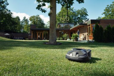 Mähroboter Ein Husqvarna Automower Mähroboter auf grünem Gras vor einem modernen Haus mit Bäumen.