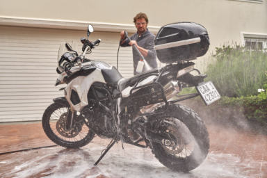 Hochdruckreiniger Mann wäscht eine weiße Reiseenduro-Motorrad mit Hochdruckreiniger.